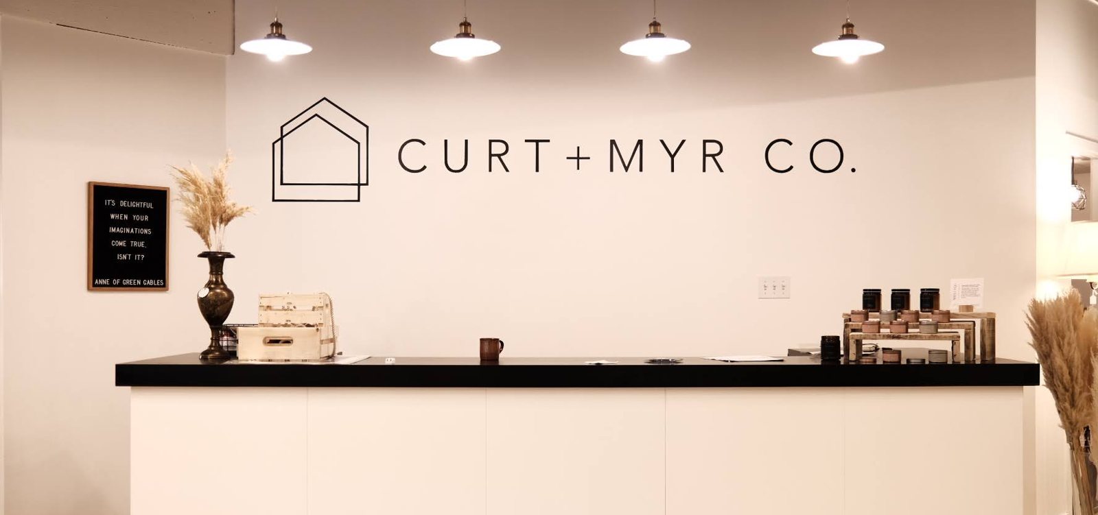 Curt + Myr Co. logo on the wall behind the shop counter, with pendant lights above